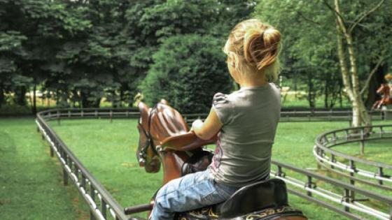 Photo prise de dos d'une enfant assise sur un des chevaux de l'attraction O'Galop du parc Bagatelle