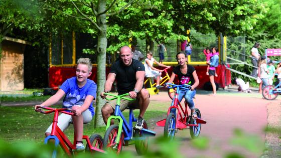 Photo d'un papa et ses enfants sur les Velos Excentriques, l'attraction historique du parc Bagatelle 